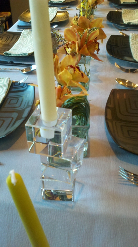 The table was decorated with a light gray table cloth, black rounded square plates, green patterned napkins, small cubes filled with copper/ brown cymbidium orchids and a few taper candles